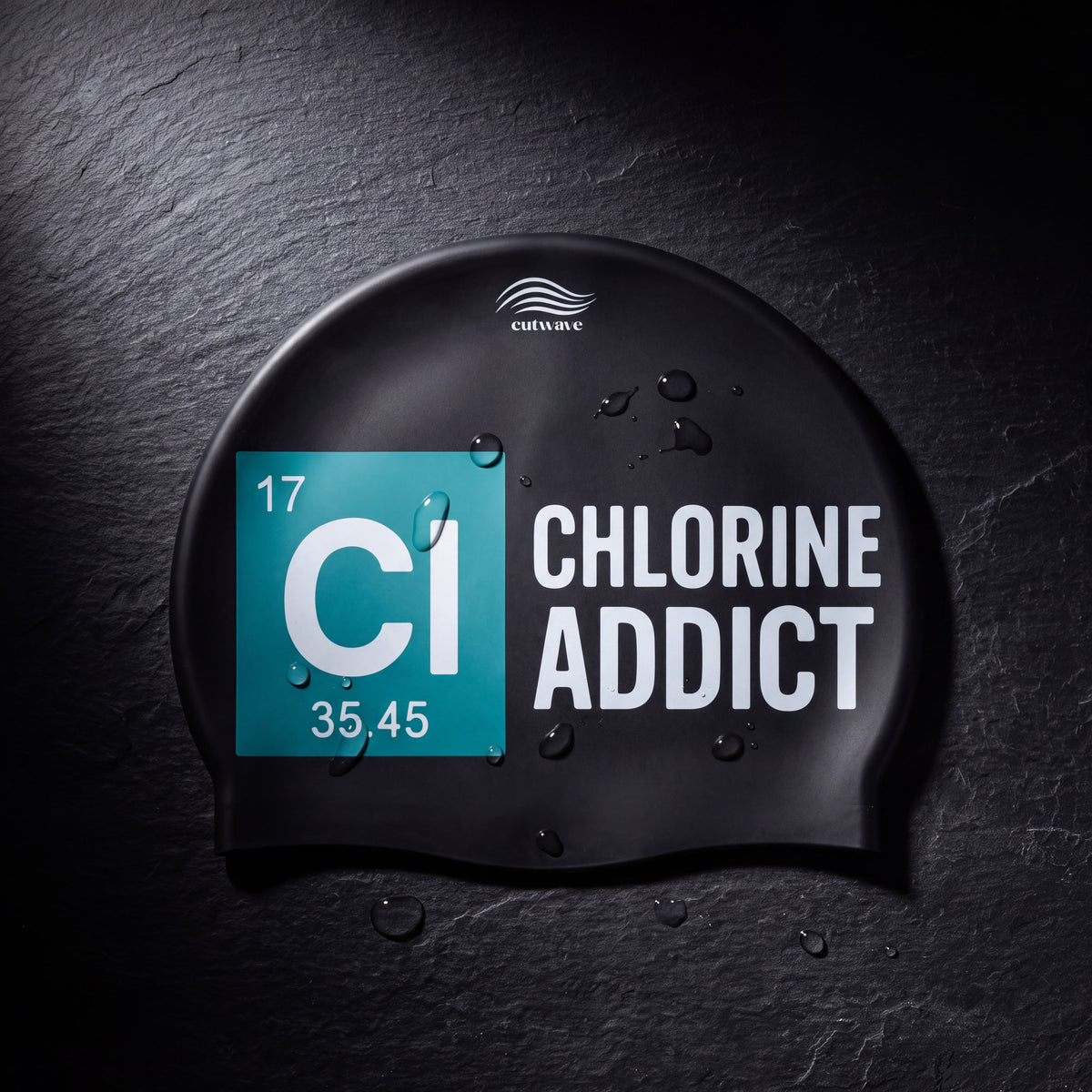 A black Chlorine Addict swim cap is laid flat with its printed design facing upward