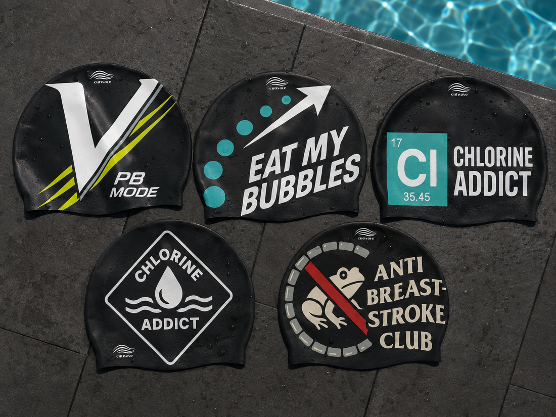 Five black CutWave silicone swim caps with printed designs lying on wet tiles beside a swimming pool.