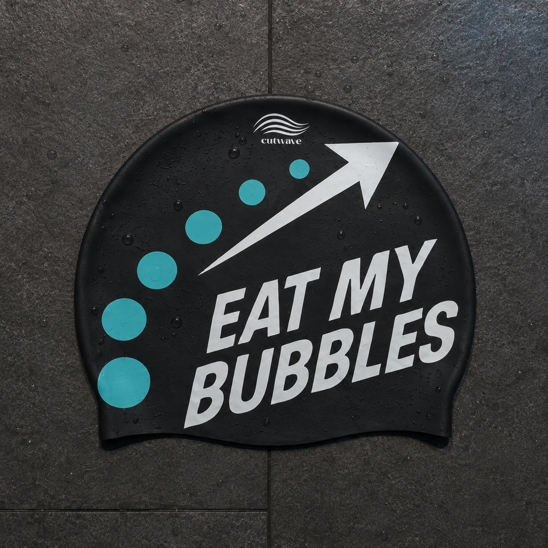 Eat My Bubbles black swim cap with teal bubbles and a white arrow.